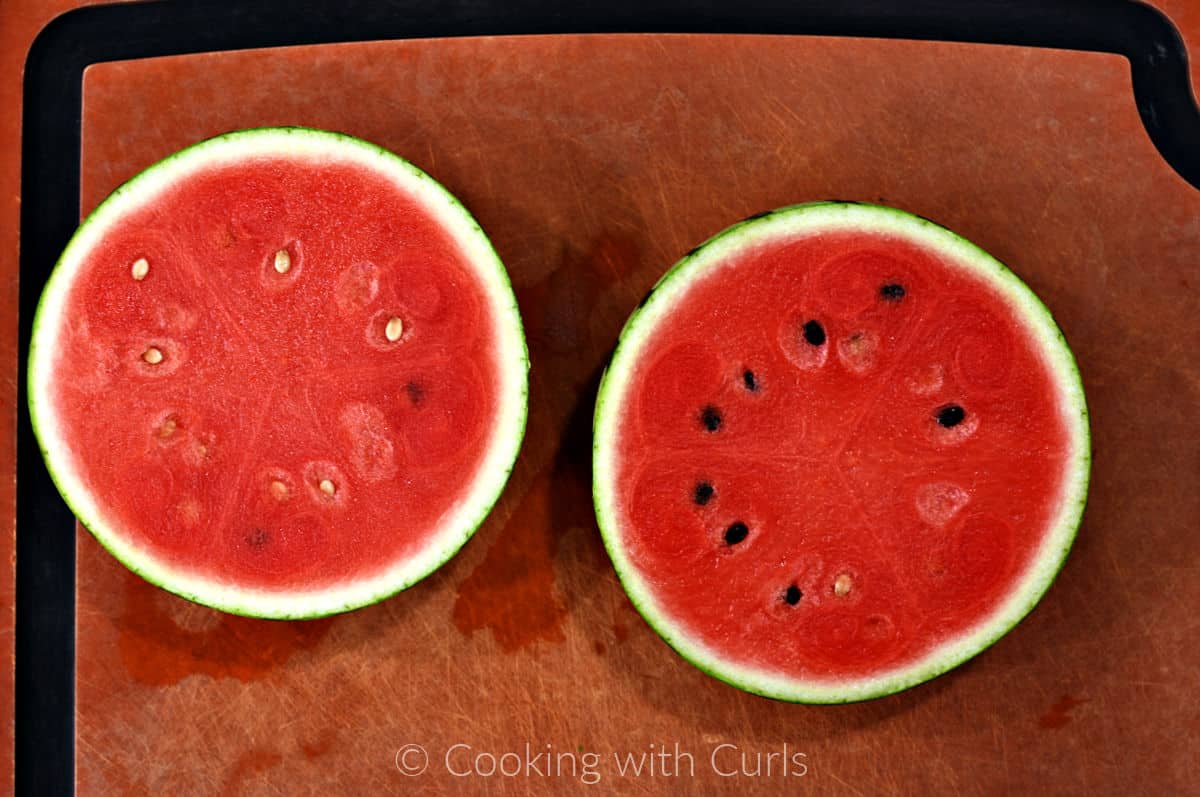 A mini watermelon cut in half on a cutting board. 