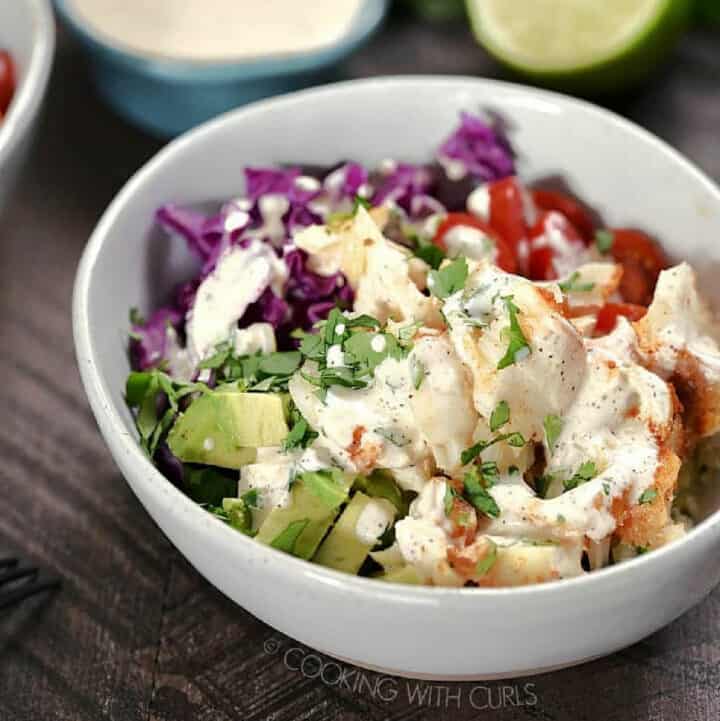 Fish, avocado, cabbage, and cilantro topped with dressing in a bowl.