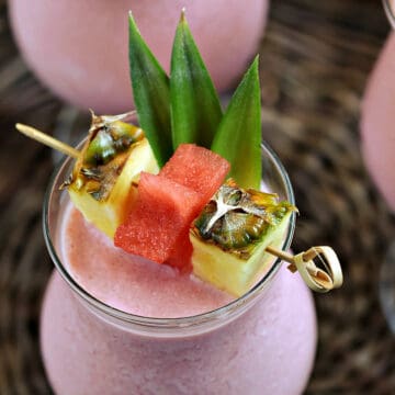 Looking down on a frozen pink drink garnished with pineapple leaves, wedges, and watermelon stars.