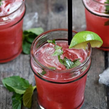 Three watermelon mojitos with lime wedges and mint leaves.