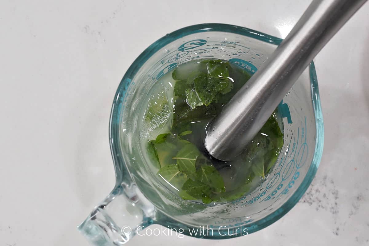 Mint leaves, crushed ice, and lime juice muddled in a glass measuring cup. 