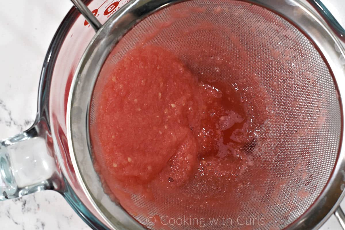 Pureed watermelon going through a fine mesh sieve into a large measuring cup.