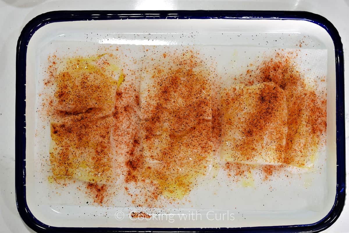 Three cod filets brushed with oil and sprinkled with taco seasoning on a platter. 