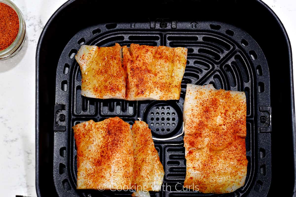 Three seasoned cod filets in an air fryer basket. 