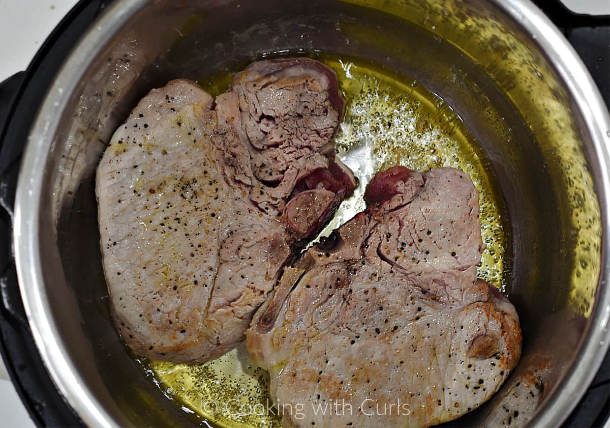 Two pork chops seared in oil inside a pressure cooker. 