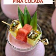 Looking down on a frozen pink drink garnished with pineapple leaves, wedges, and watermelon stars with title graphic across the top.