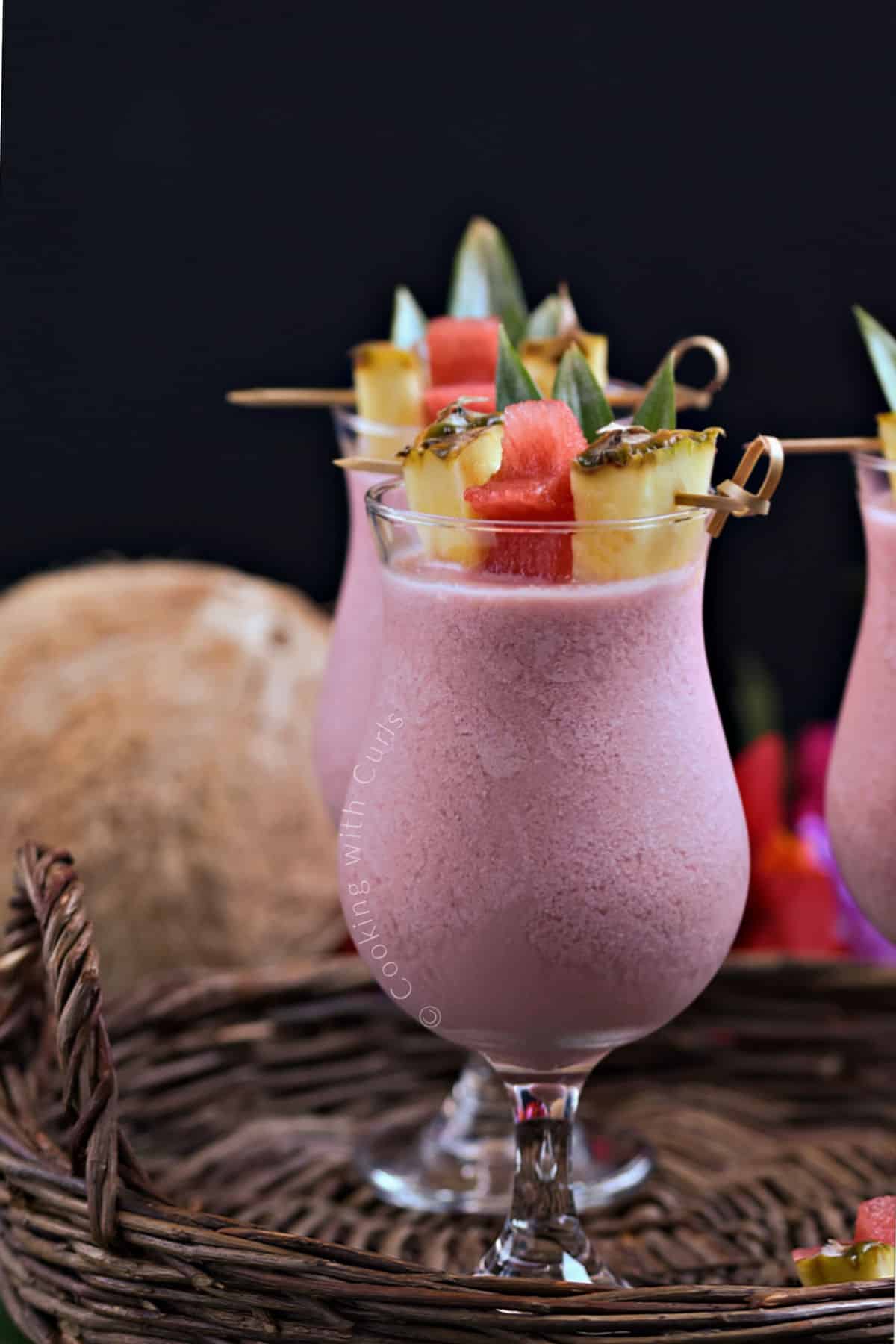 Looking at the sides of three cocktail glasses filled with a frozen pink drink garnished with pineapple wedges, leaves, and watermelon stars.