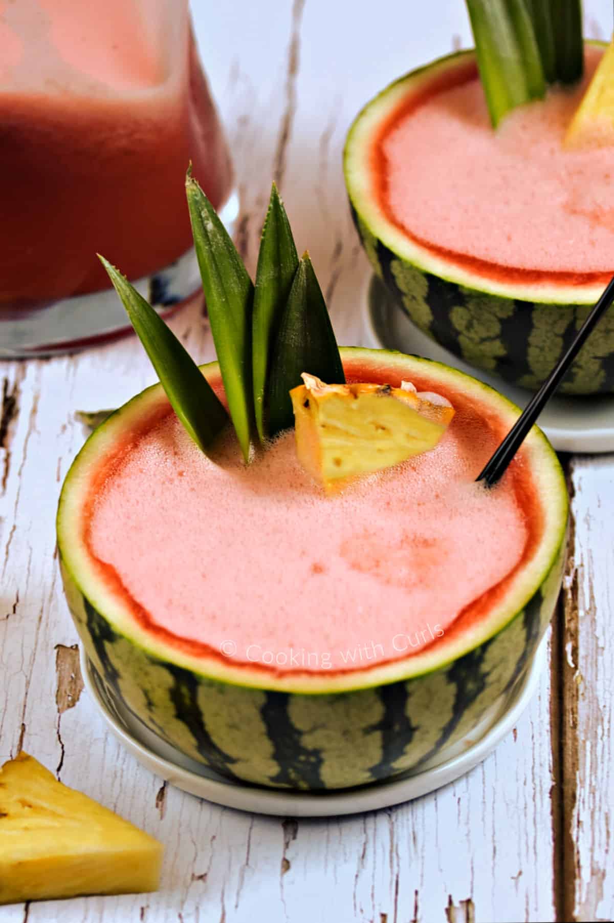 Pink watermelon rum punch served in two hollowed out watermelons garnished with pineapple leaves and wedges.