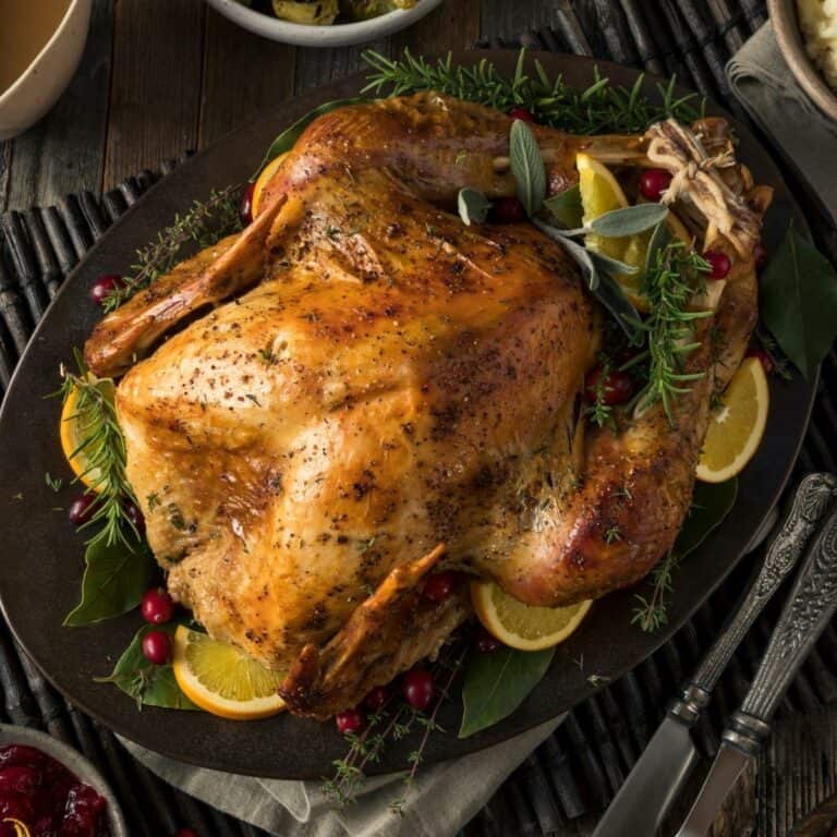 A Thanksgiving turkey on a platter with herbs and orange slices.