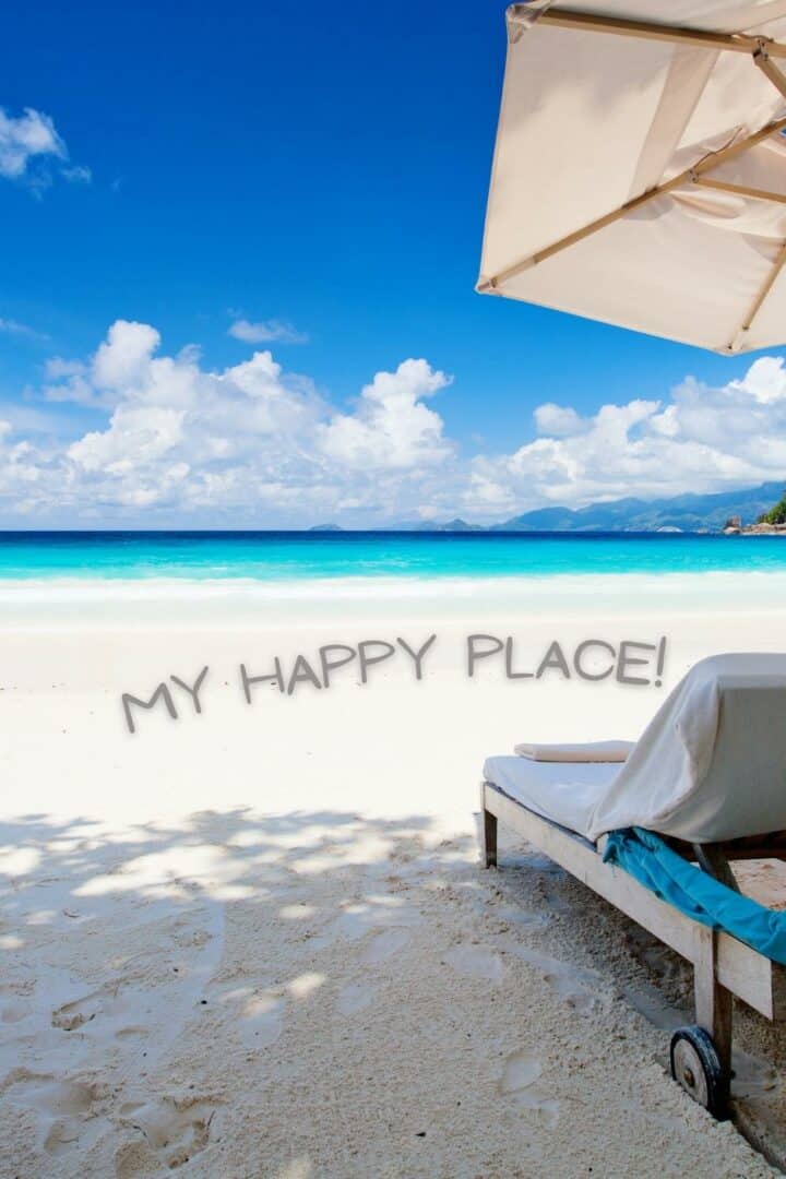 A beach lounger on a sandy beach with my happy place! written over the sand.