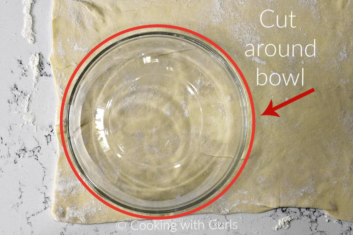 A small bowl on a sheet of puff pastry used as a template to cut out a circle. 