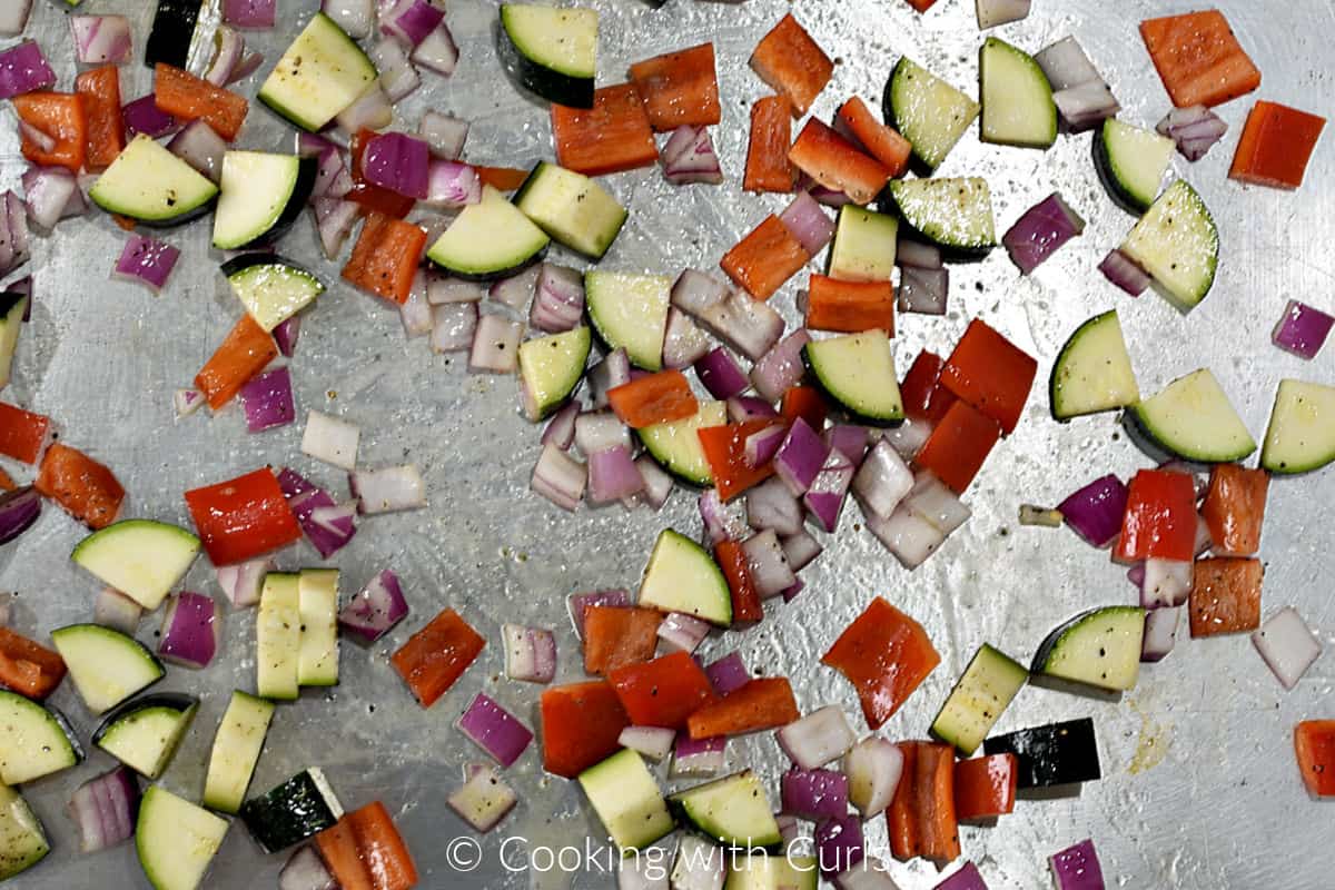 Chopped zucchini, red pepper and diced red onions seasoned on a baking sheet. 
