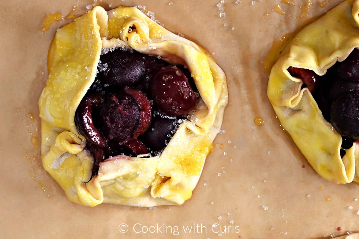 Egg wash on two puff pastry cherry tarts with sugar on one. 