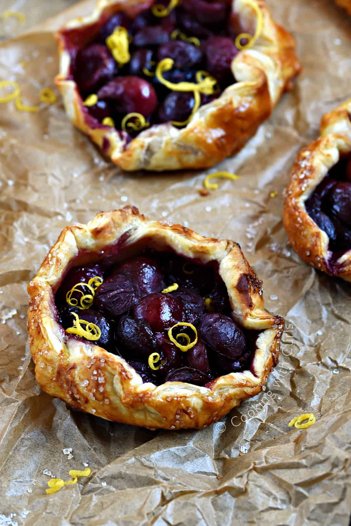 TwoFresh Cherry Tarts with Puff Pastry on a sheet of parchment paper.