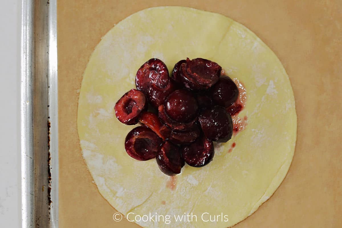 Fresh cherries in the center for a puff pastry circle on a parchment lined baking sheet. 