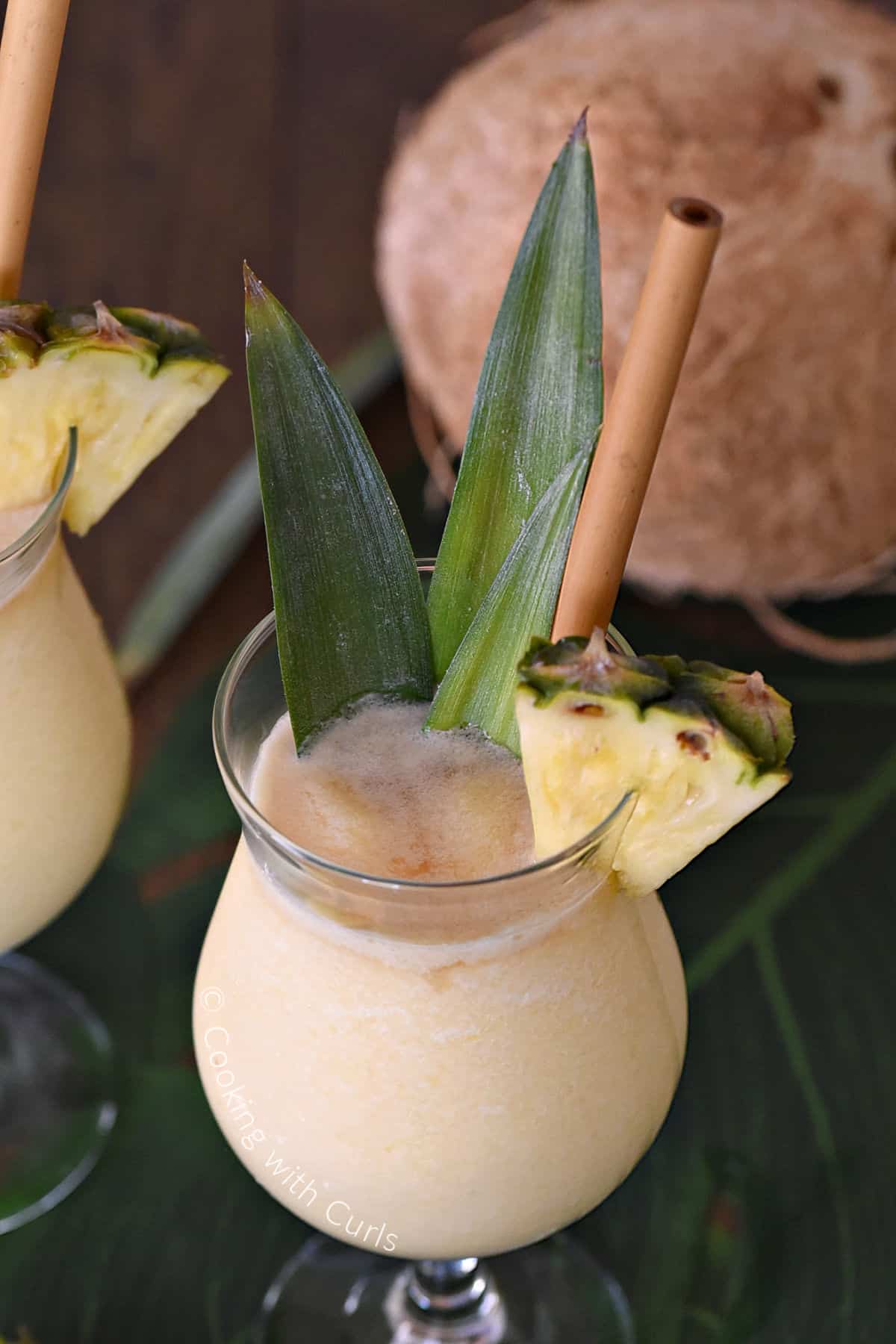 Pina Colada topped with dark rum and garnished with pineapple leaves and wedge with a coconut in the background. 
