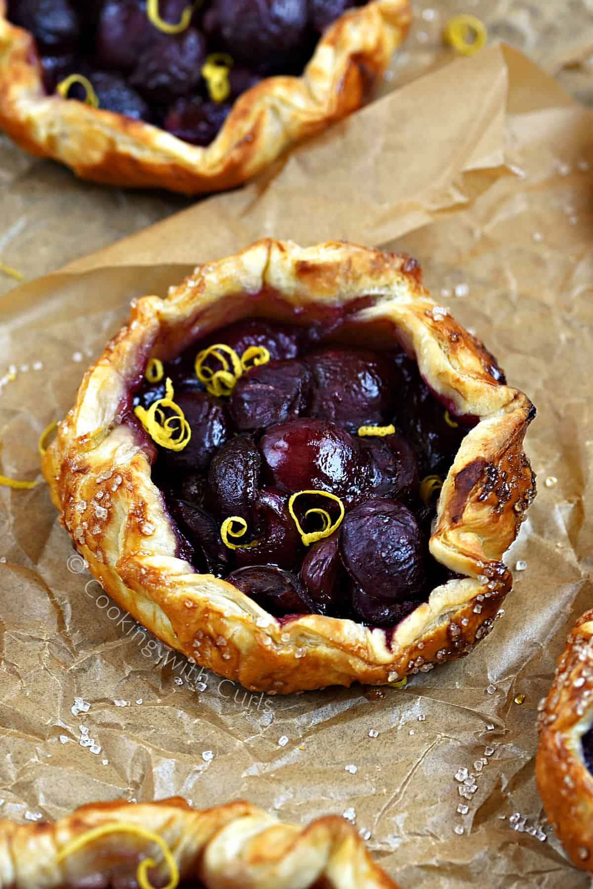 Four Puff Pastry Cherry Tarts on a sheet of parchment paper.