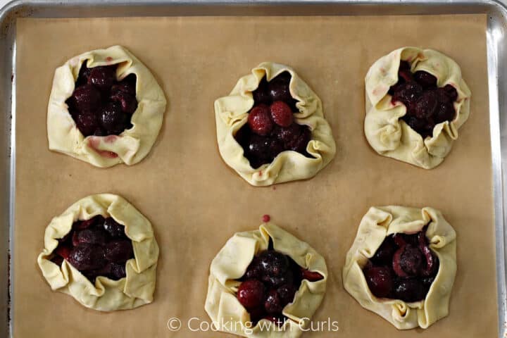 Six puff pastry cherry tarts folded and ready to go into the refrigerator.