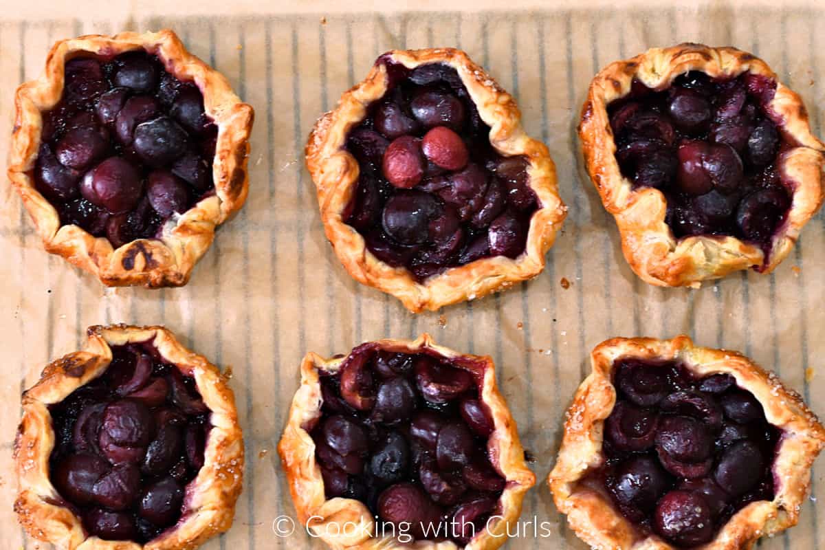 Six puff pastry cherry tarts on a wire cooling rack. 