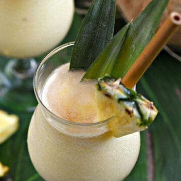 Looking down on two cocktail glasses filled with frozen Pina colada with dark rum floating on top and pineapple wedge and leaves as garnish.