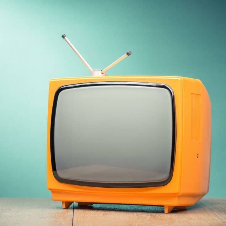 Vintage orange TV with teal wall behind.