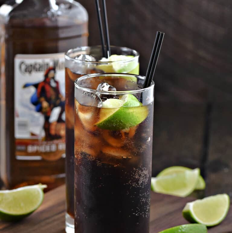 Two tall glasses filled with dark rum, cola, and ice cubes with a lime wedge garnish.