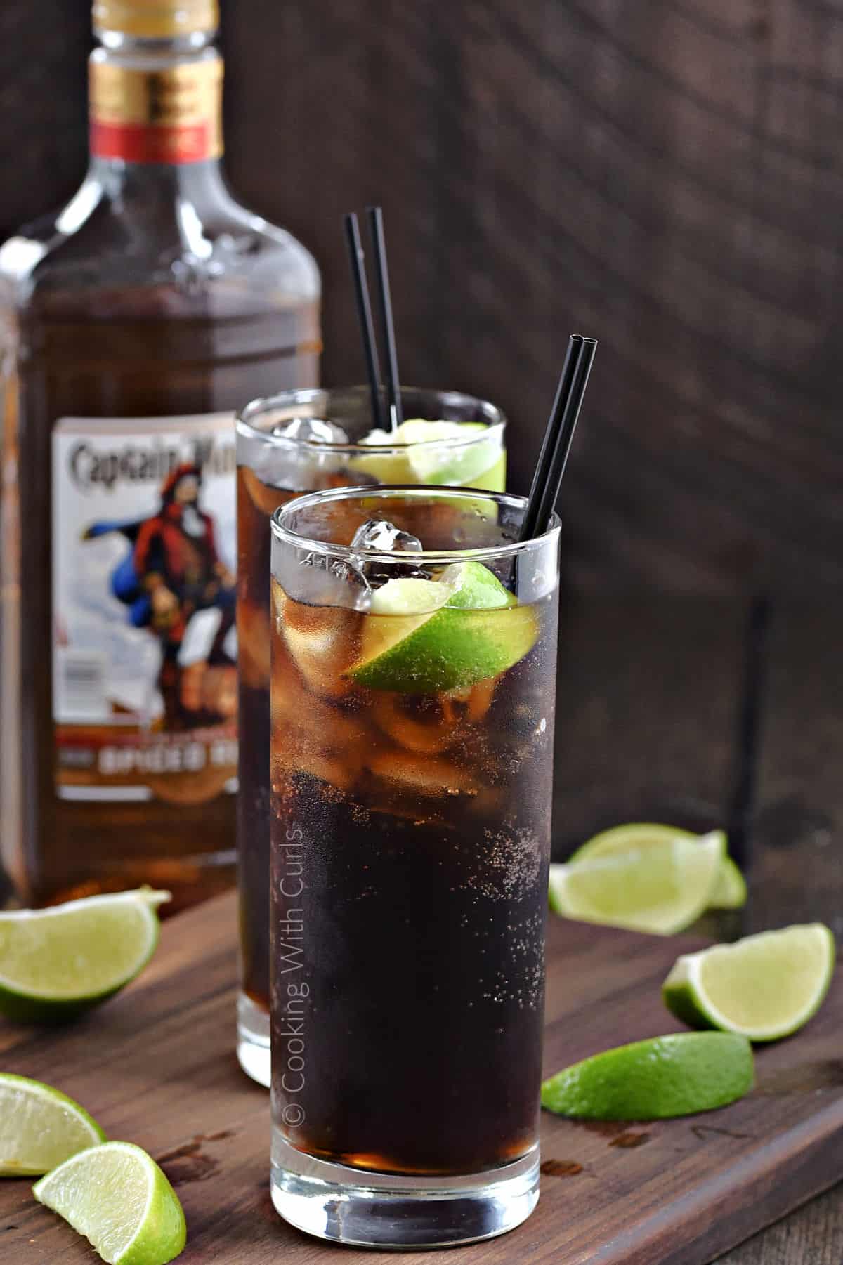 Two tall glasses filled with dark rum, cola, and ice cubes with a lime wedge garnish.