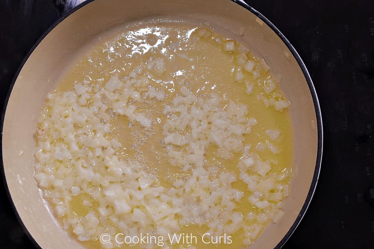 Diced onion simmering in butter inside a skillet. 