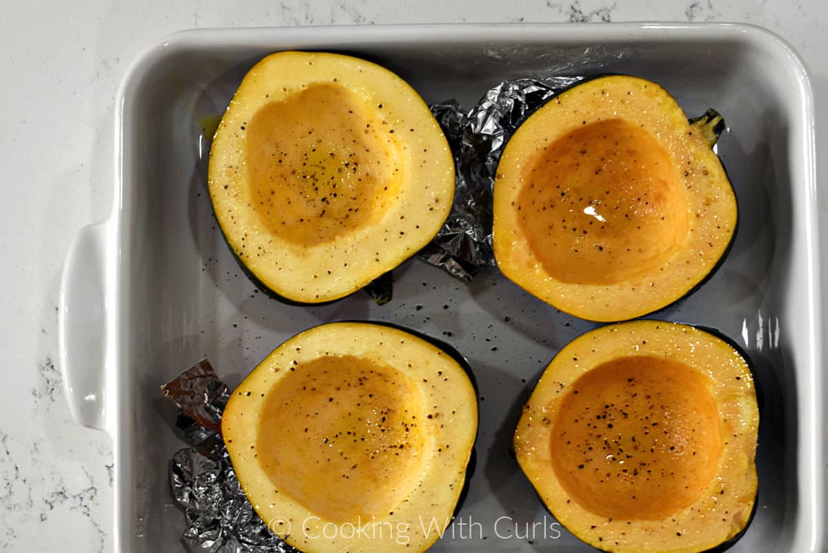 Four acorn squash halves in a baking dish brushed with oil and sprinkled with salt and pepper. 
