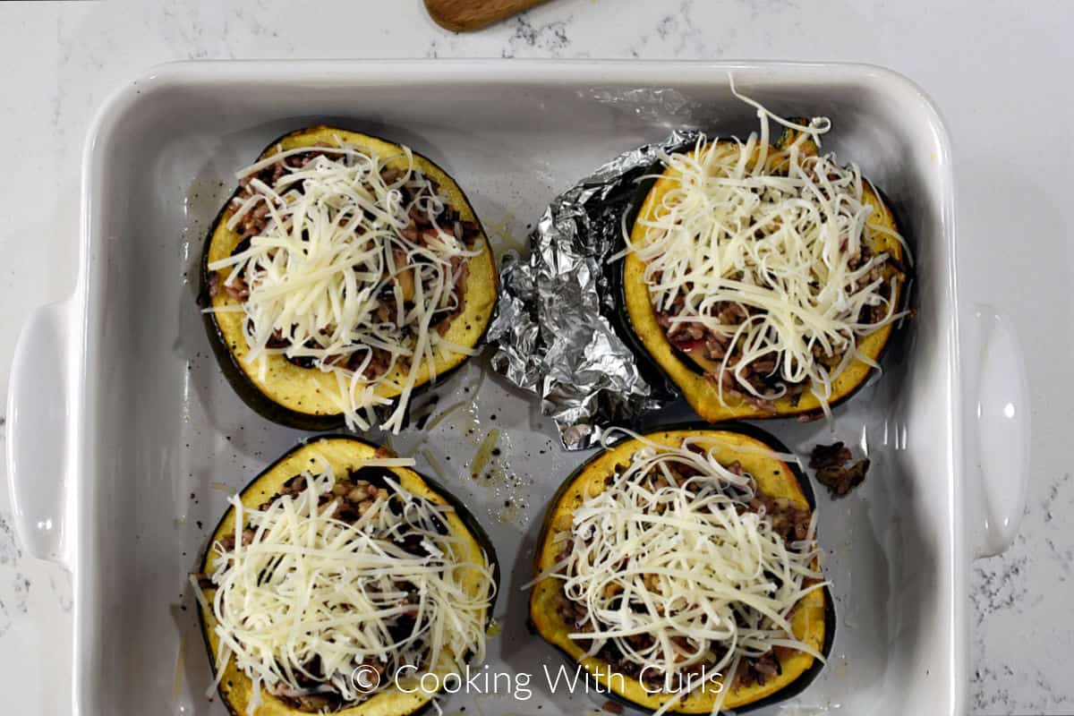 Four acorn squash halves in a baking dish filled with rice mixture and covered with grated cheese. 