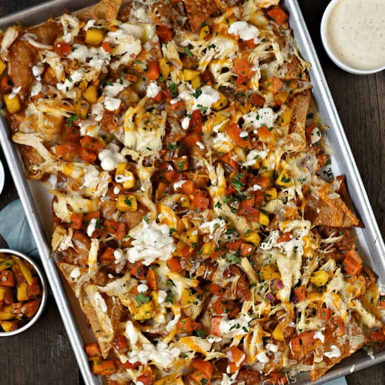 Looking down on a sheet pan filled with wonton chips topped with Asian chicken, papaya mango salsa and drizzled with sauce recipe.