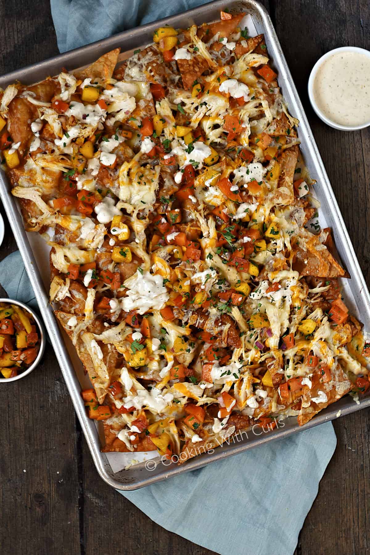 Looking down on a sheet pan filled with wonton chips topped with Asian chicken, papaya mango salsa and drizzled with sauce recipe. 