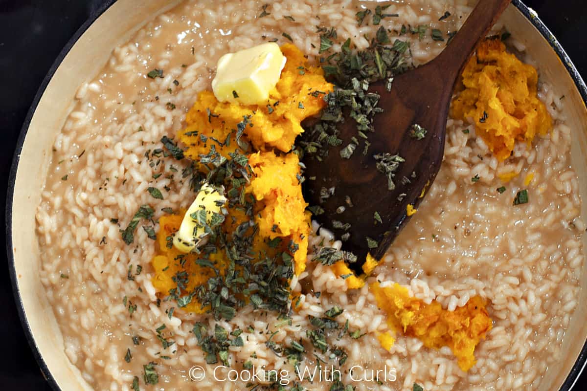 Mashed butternut squash, butter, and chopped sage leaves on the rice mixture in a skillet. 