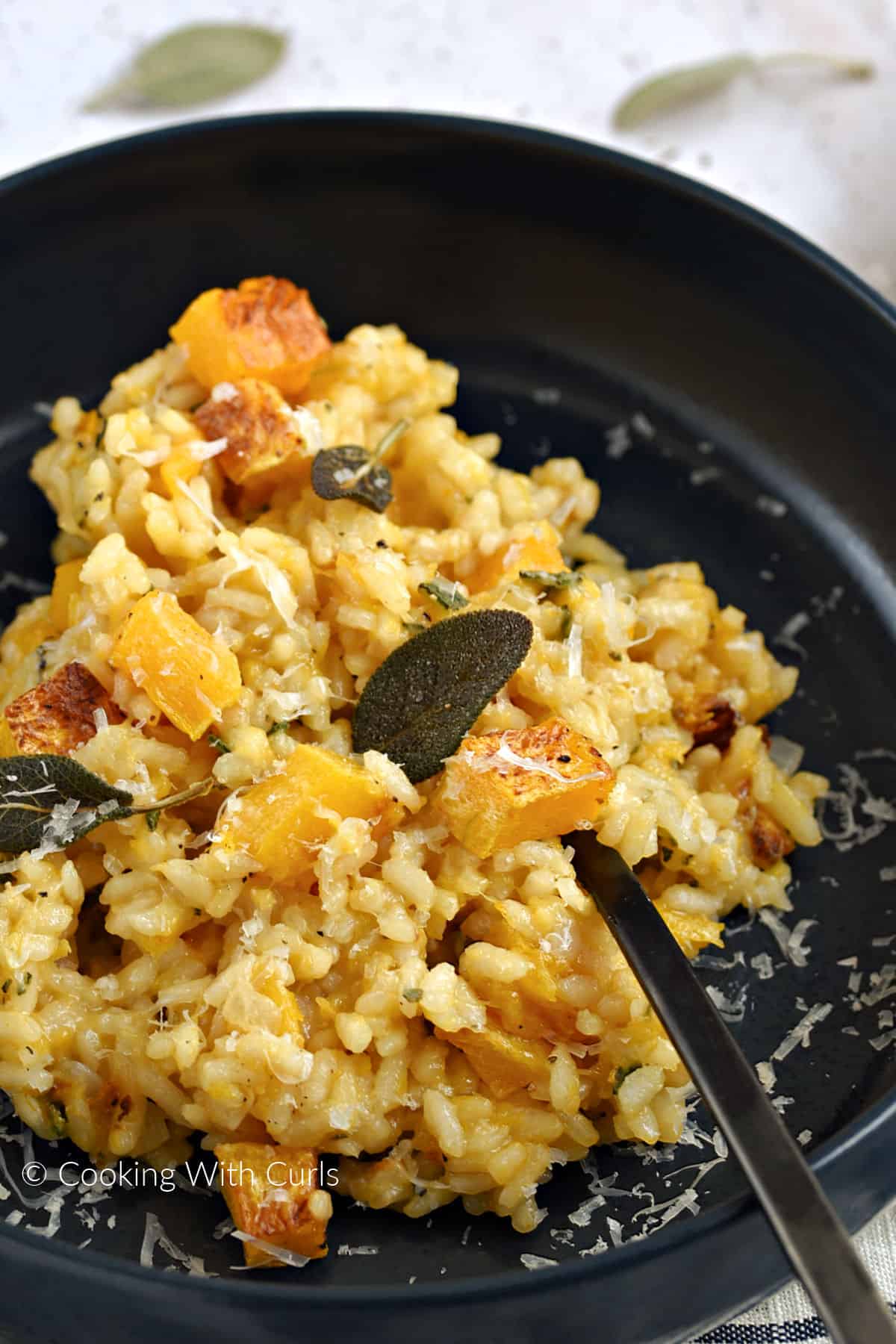 Risotto and butternut squash cubes in a blue bowl topped with crispy sage leaves and parmesan cheese. 