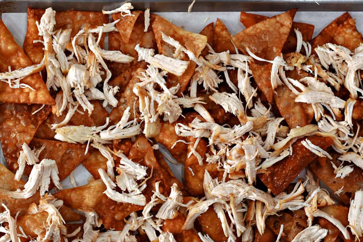Shredded chicken on top of wonton chips on a baking sheet. 