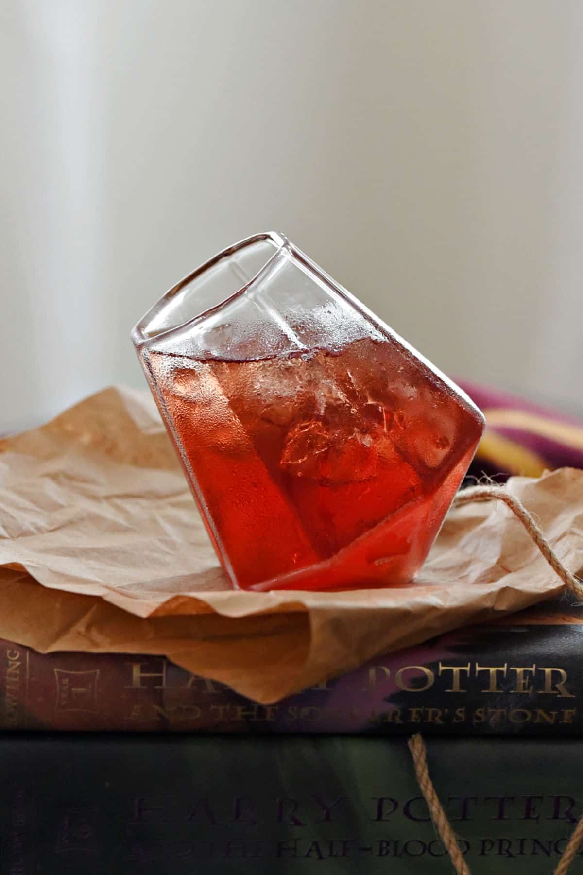 Red cocktail in a square cut glass sitting on brown paper in front of Harry Potter books.