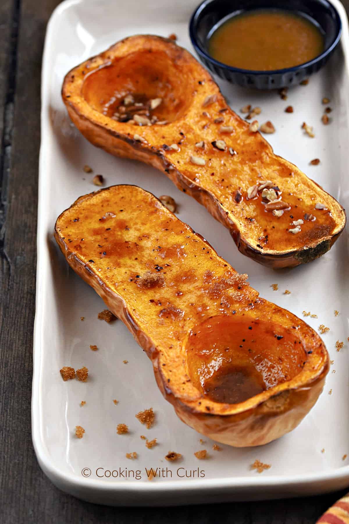 Two air fryer butternut squash halves on a rectangle platter, one with maple syrup and chopped pecans, the other with melted butter and brown sugar. 