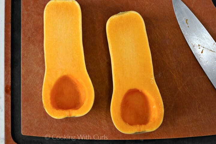 Two butternut squash halves with the seeds and pulp removed on a cutting board. 
