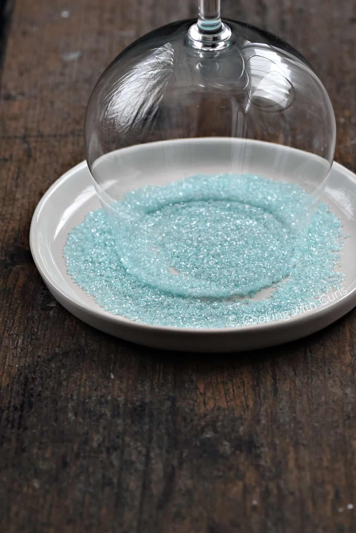 A glass goblet rim side down in a small plate of blue sugar. 