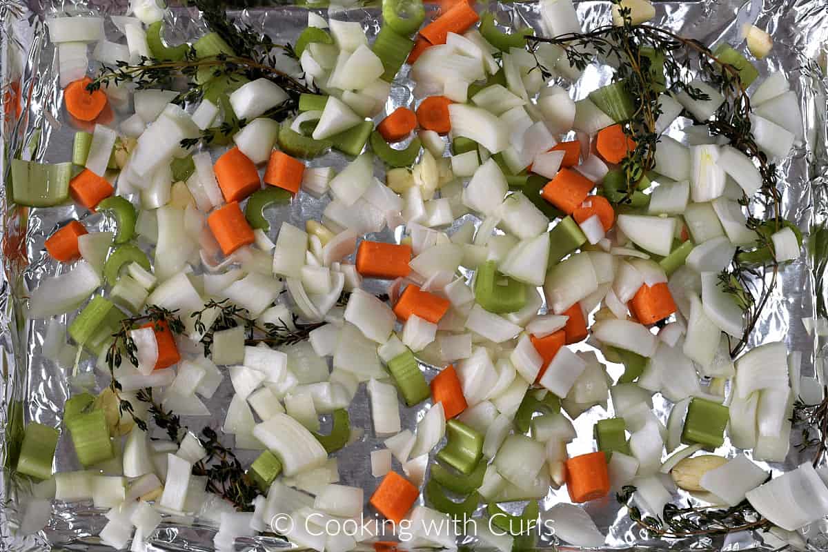 Chopped onion, celery, carrots, thyme sprigs and garlic cloves on a foil lined baking sheet. 