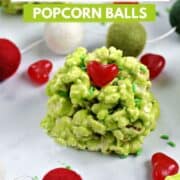 A green marshmallow popcorn ball with a red candy heart and green sprinkles surrounded by sprinkles, hearts, and colorful ball garland with title graphic across the top.