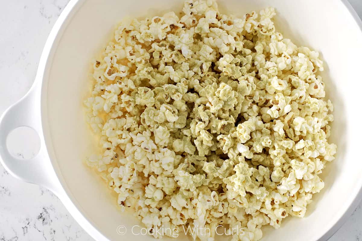 Popped popcorn with wasabi mixture on top in a large mixing bowl. 