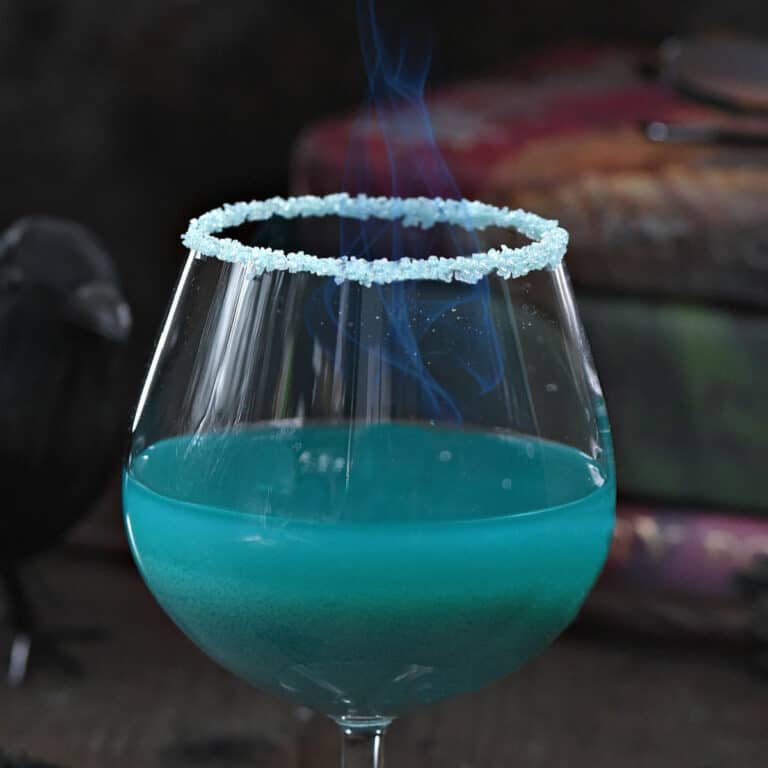 Teal blue Goblet of Fire cocktail recipe in a goblet glass with flames in front of a stack of Harry Potter books.