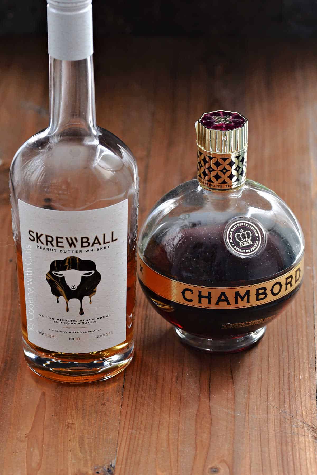 A bottle of Skrewball peanut butter whiskey and a bottle of chambord liqueur on a wooden board.