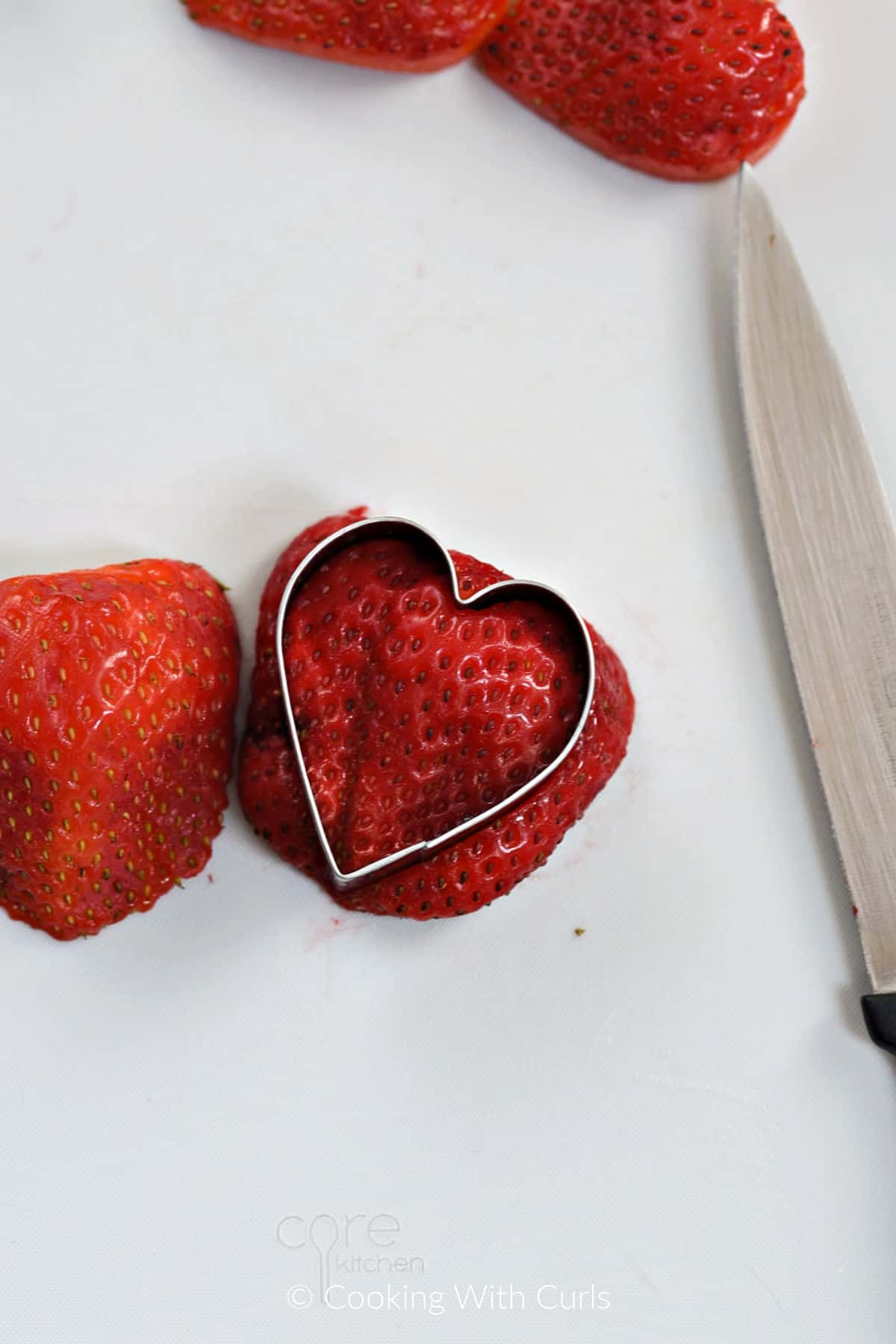 A heart shaped cookie cutter pushed into one half of a strawberry slice. 