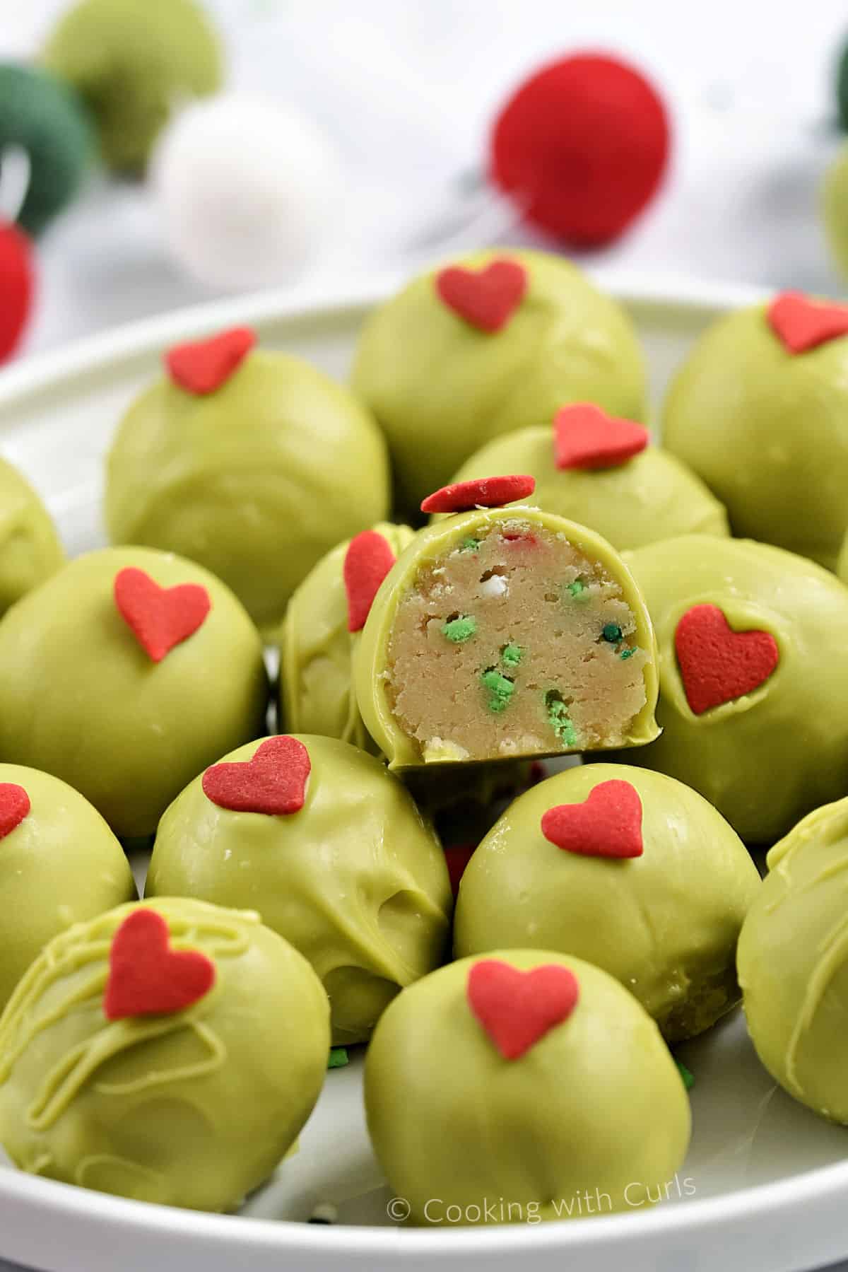 A plate filled with green chocolate coated oreo balls decorated with red candy hearts and one cut in half to show the inside. 
