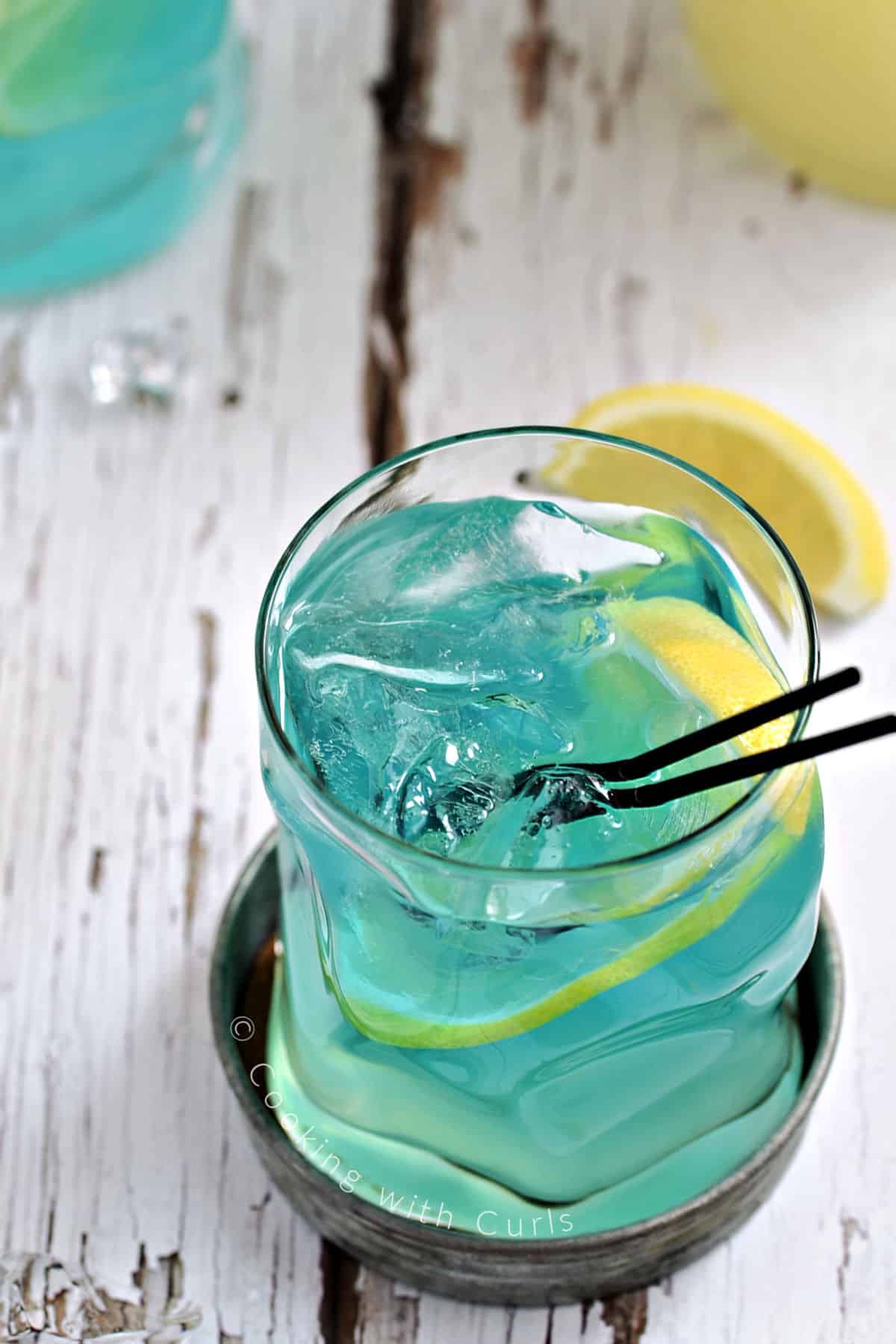 Bright electric blue drink in a cocktail glass garnished with lemon slices.