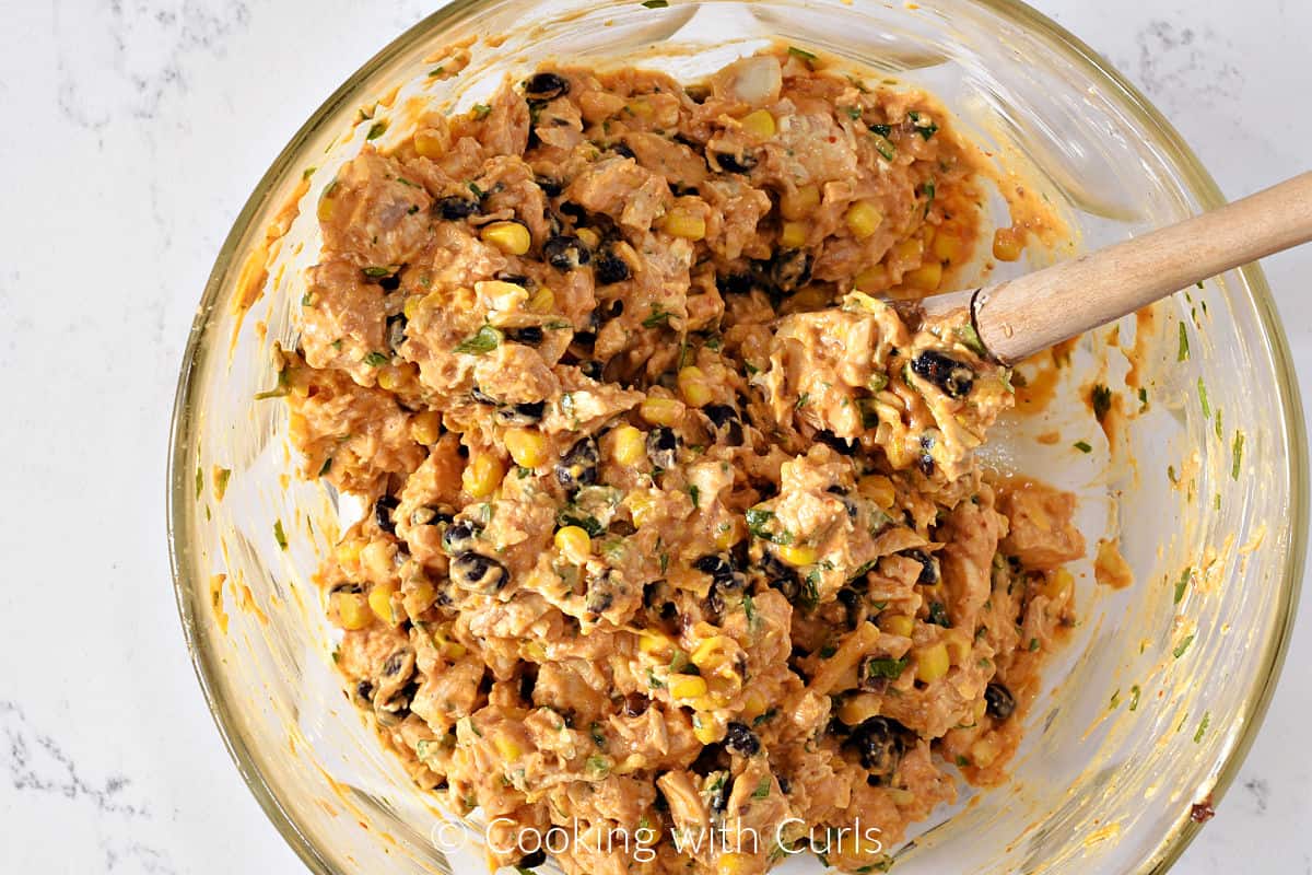 Creamy turkey filling mixed in a bowl with red enchilada sauce, corn, black beans, cilantro, and diced jalapeno. 