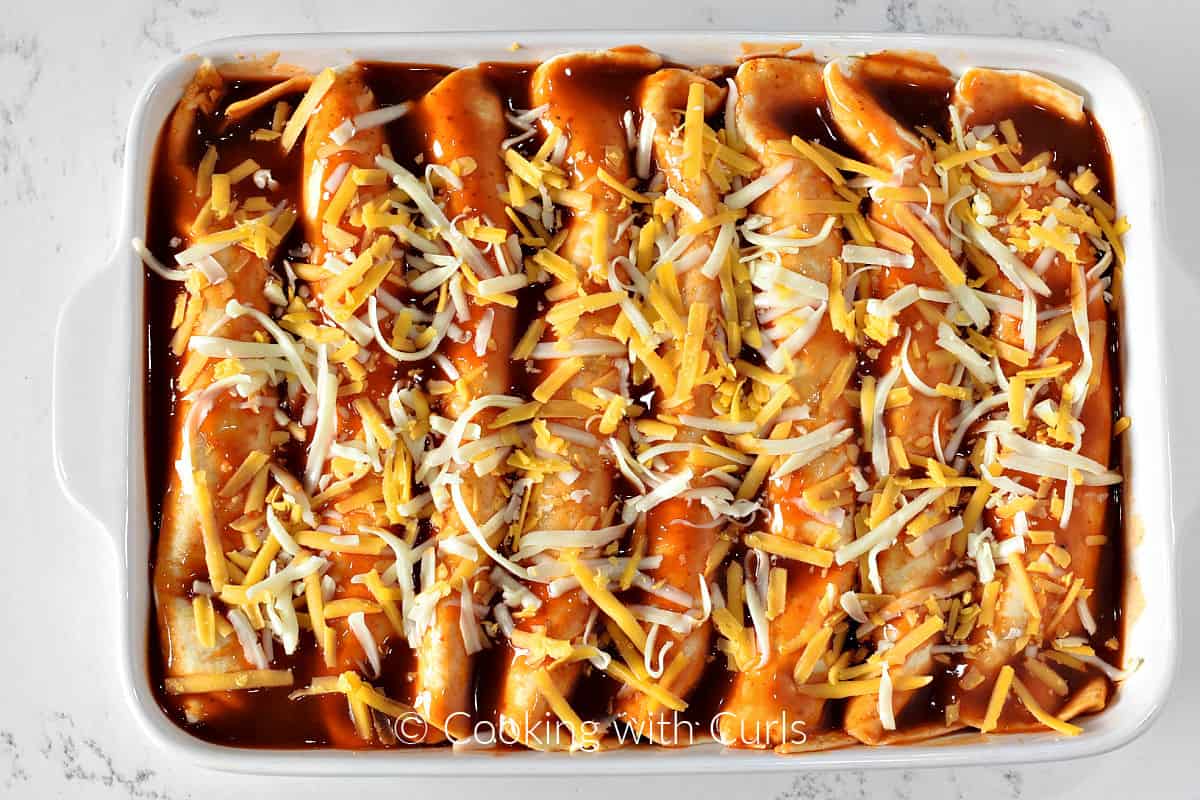 Eight rolled enchiladas in a baking dish covered with red sauce and shredded cheese. 