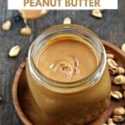 Homemade Peanut Butter in a square jar on a wood plate surrounded by peanuts with title graphic across the top.